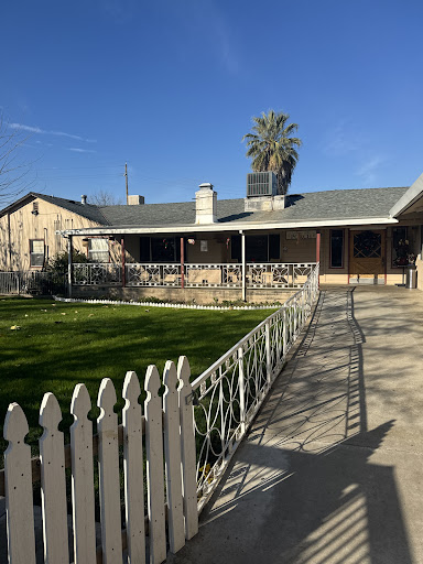 A charming single-story house with a white picket fence and a palm tree in the front yard.