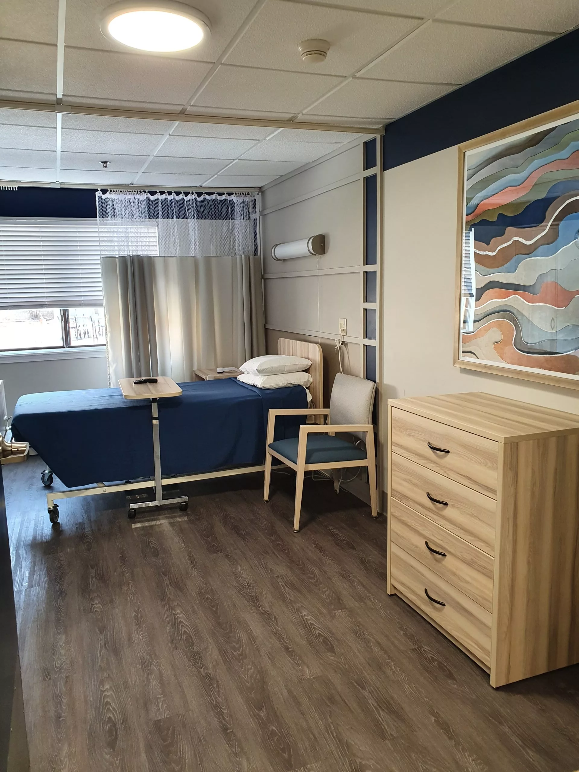 A well-arranged hospital room with a patient bed, chair, and dresser, featuring modern interior design elements.