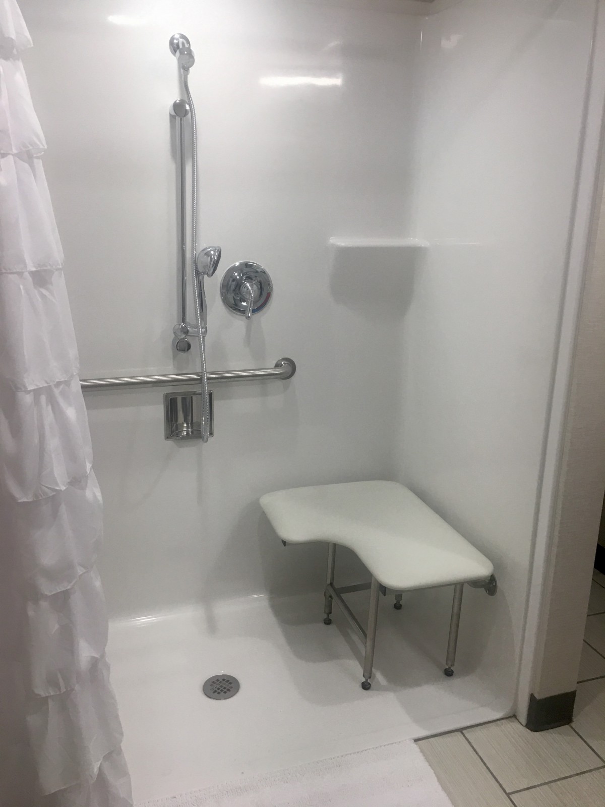 A bathroom with an accessible shower featuring a foldable bench and grab bar.
