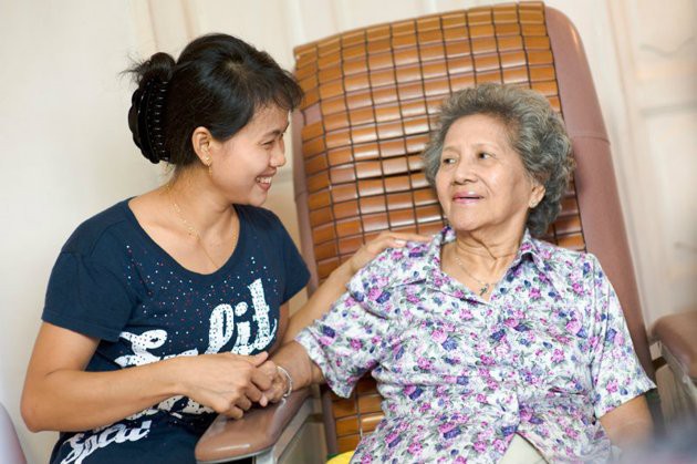 A young woman provides support and companionship to an elderly woman, sharing a moment of joy together.