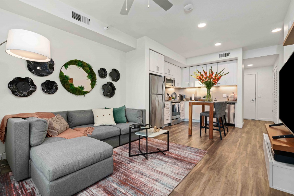 A modern open-concept living room and kitchen area, featuring an L-shaped sofa, wooden flooring, and stylish decor.