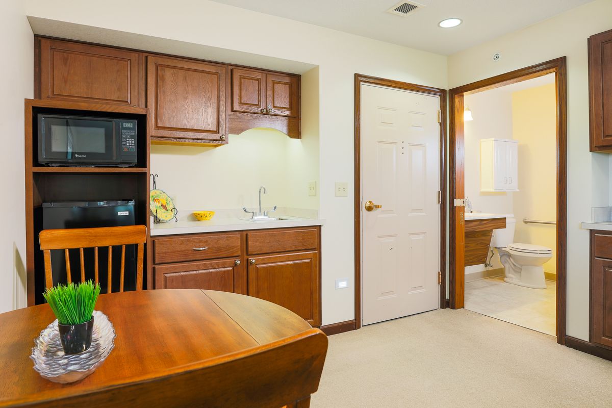 A cozy kitchenette with a dining table, featuring wooden cabinets and a microwave.