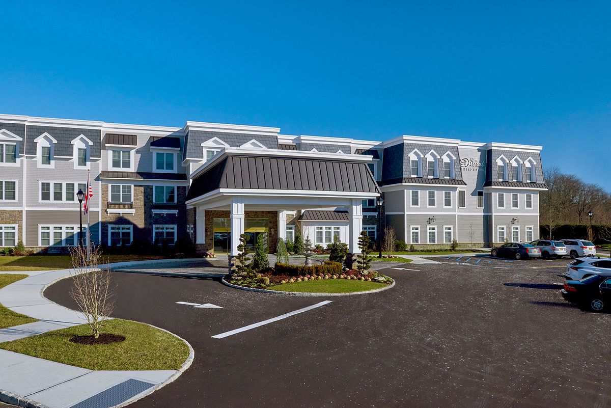 A modern residential building with a landscaped entrance and clear blue sky.