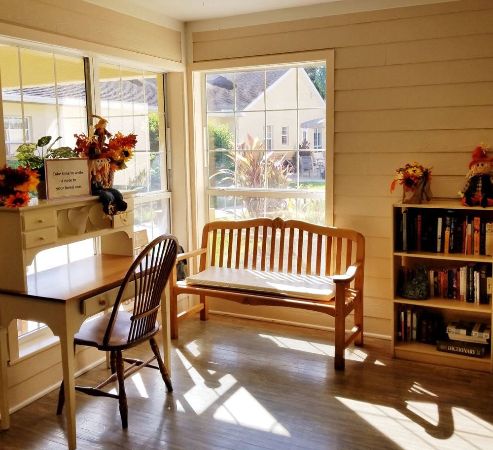 A cozy sunlit room with wooden furniture and a bookshelf, offering a peaceful window view.