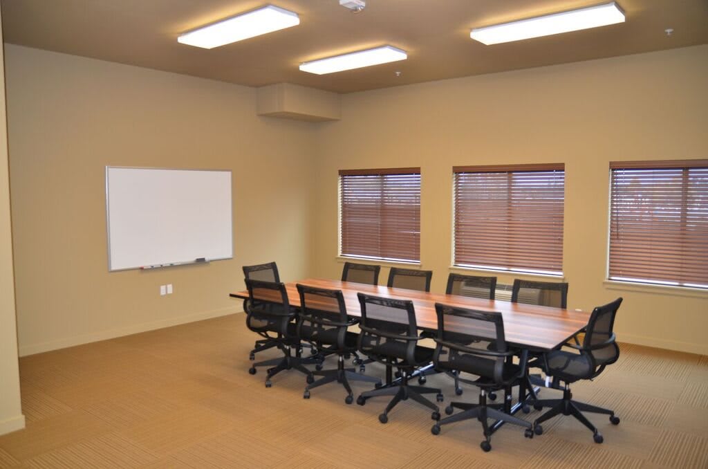 A modern conference room setup with a long table, multiple chairs, and a whiteboard.