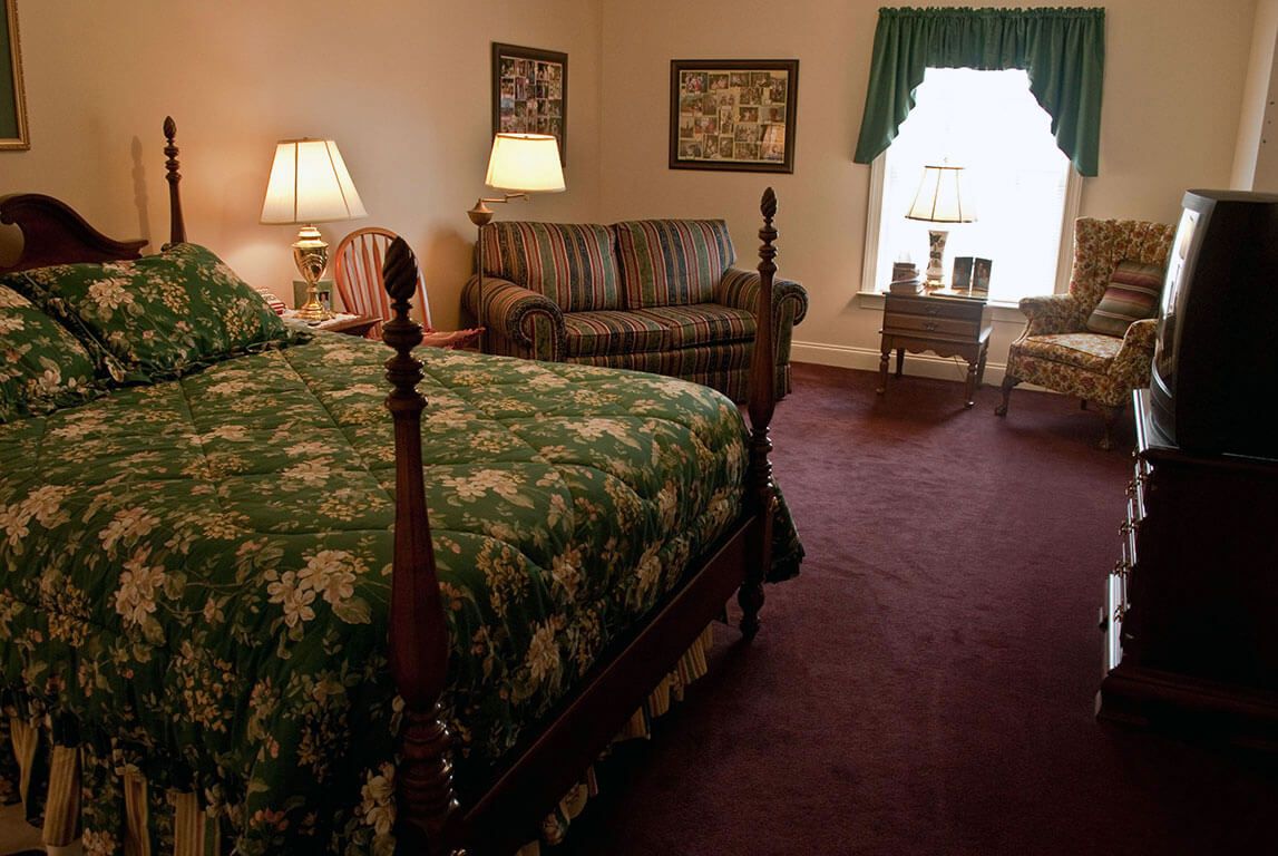 A cozy bedroom with traditional decor, featuring a large bed, lamps, a sofa, and a window.