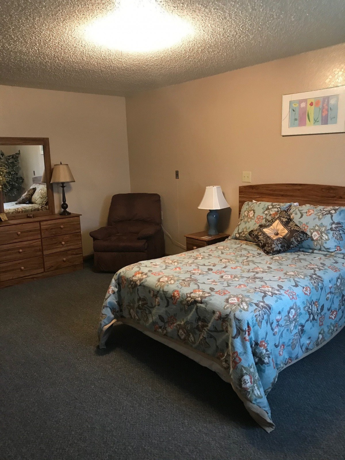 A cozy bedroom with a bed, armchair, dresser, and decorative elements.