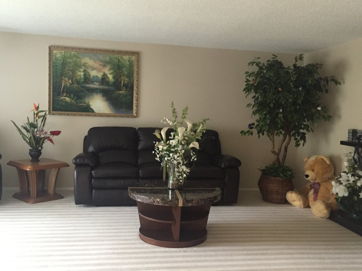 A cozy living room with a dark sofa, a coffee table decorated with flowers, and a painting on the wall.