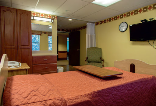 A cozy hotel room featuring a bed with an orange cover, a mirror, and a green chair.