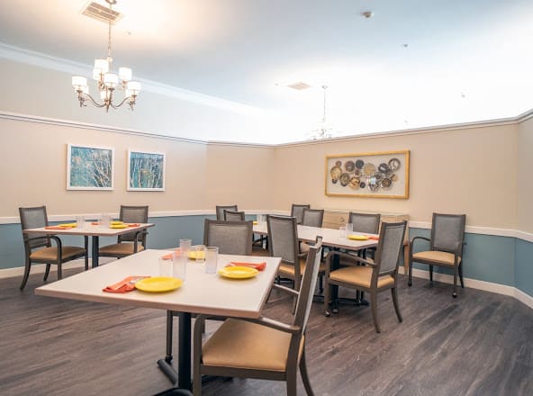 A well-lit dining room with neatly arranged tables and chairs, adorned with artwork on the walls.