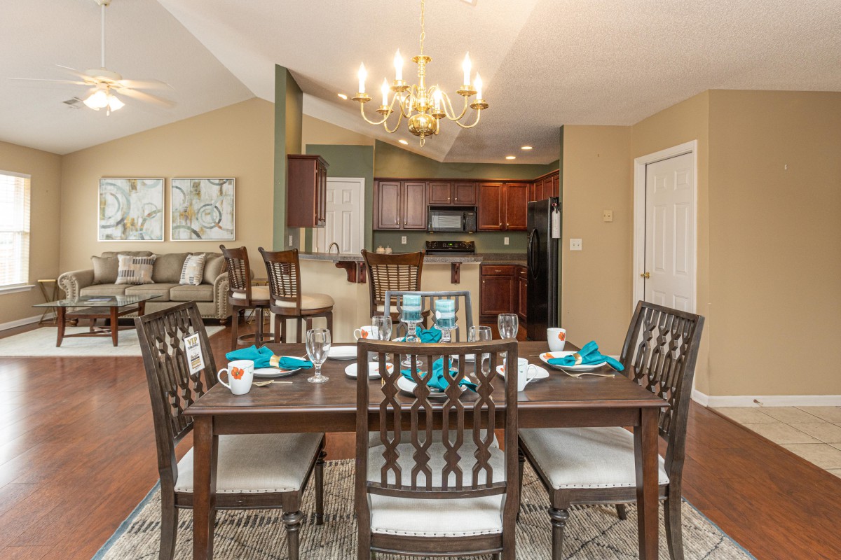 A stylish dining area with a set table, adjacent to a modern kitchen, illuminated by an elegant chandelier.