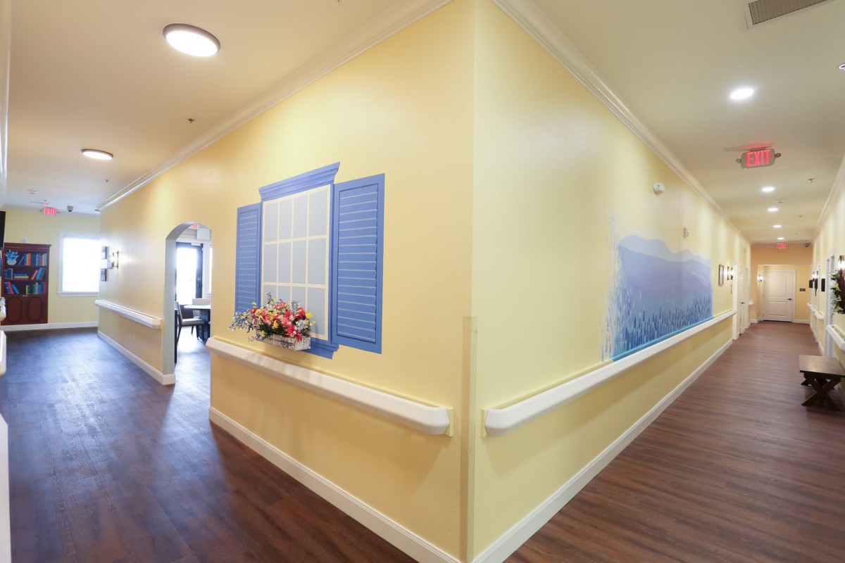 A hallway with yellow walls and blue decorative shutters, featuring a wooden floor and handrails.