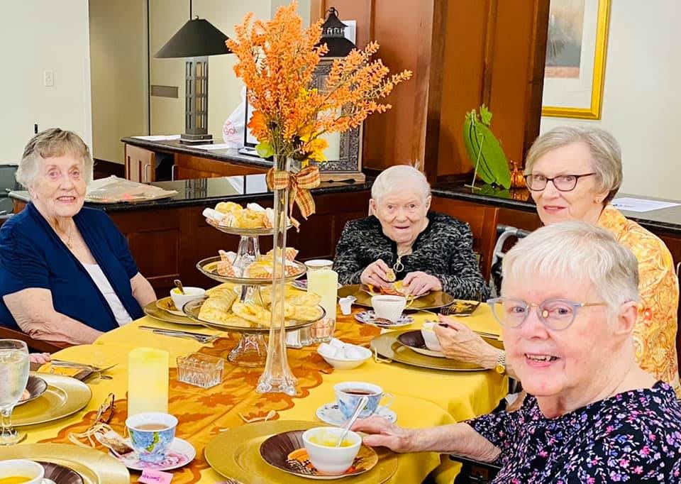 A group of elderly women enjoying a tea party with autumn-themed decor.