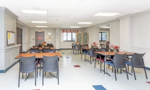 A bright community room with tables and chairs arranged neatly, featuring decorative elements and colorful floor tiles.