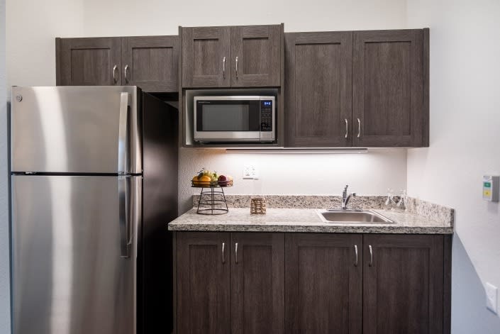 A modern kitchen with dark cabinets, a stainless steel refrigerator, microwave, and sink.