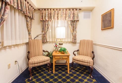 A traditional interior setting with two striped chairs and a wooden table, illuminated by a lamp.