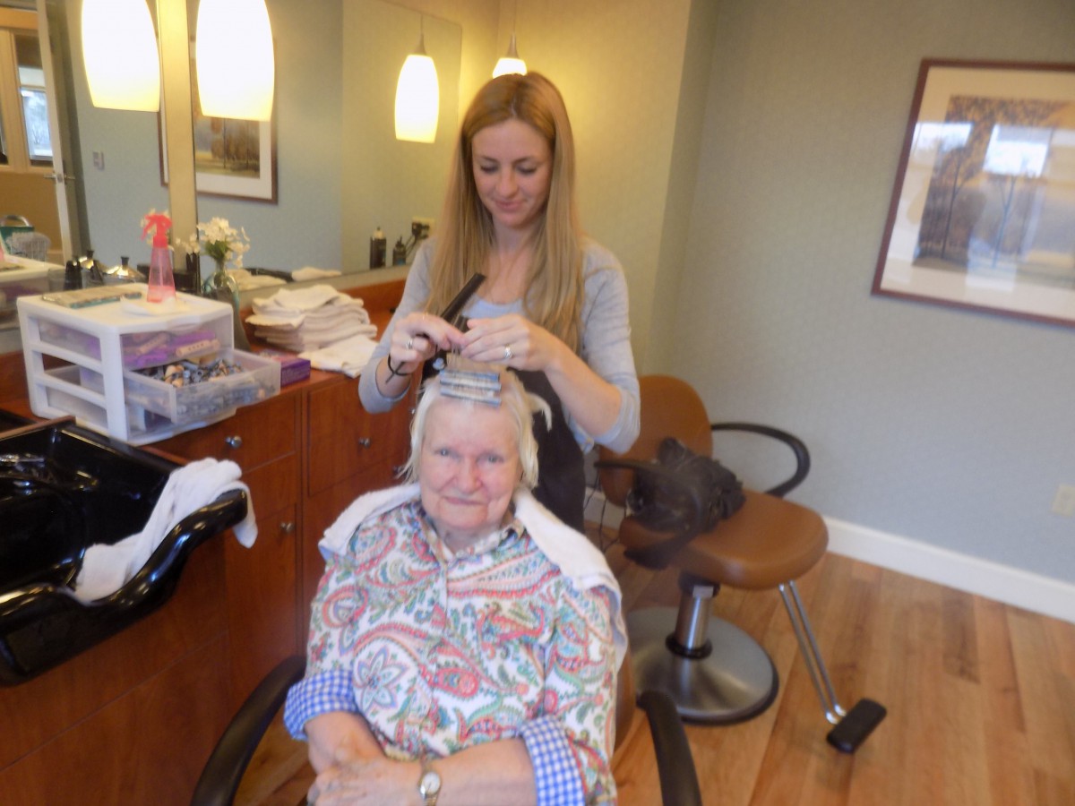 A hairstylist working on a senior woman's hair in a salon.