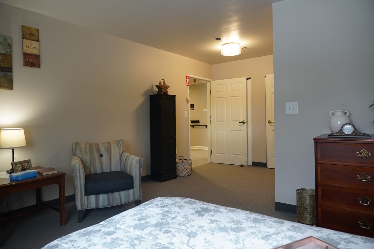 A cozy bedroom featuring a striped chair, tall cabinet, and visible doorway.