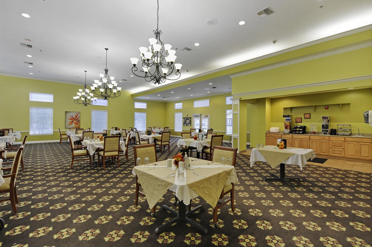 An elegant dining room with yellow walls and chandeliers, featuring several tables and chairs arranged neatly.