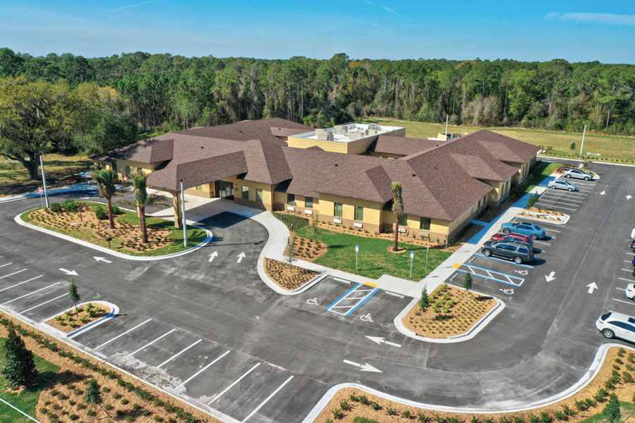 Aerial view of a building with surrounding parking lots and landscaped areas on a sunny day.