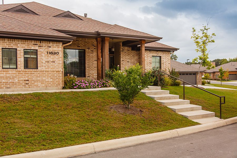 A suburban brick house with a well-maintained front yard and concrete stairs leading to the entrance.