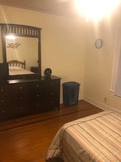 A cozy bedroom with a dresser, mirror, and bed on hardwood flooring.