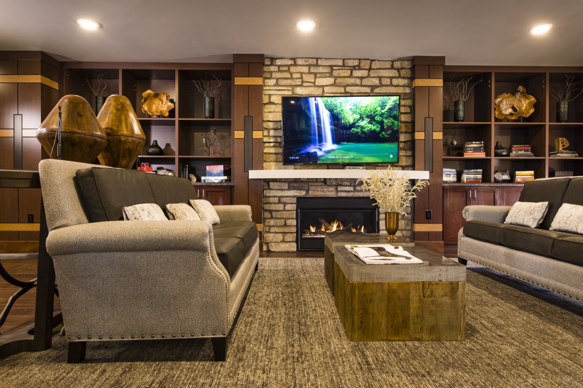 A modern living room featuring a cozy fireplace, a large television mounted on a brick wall, comfortable sofas, and stylish bookshelves.