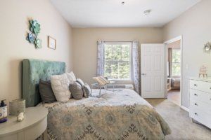 A cozy bedroom with a large bed covered in decorative pillows, a patterned blanket, and natural light streaming through the window.