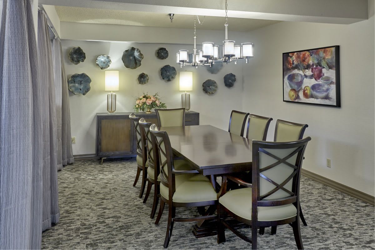 A well-decorated dining room with a long table and elegant chairs, featuring stylish lighting and wall art.