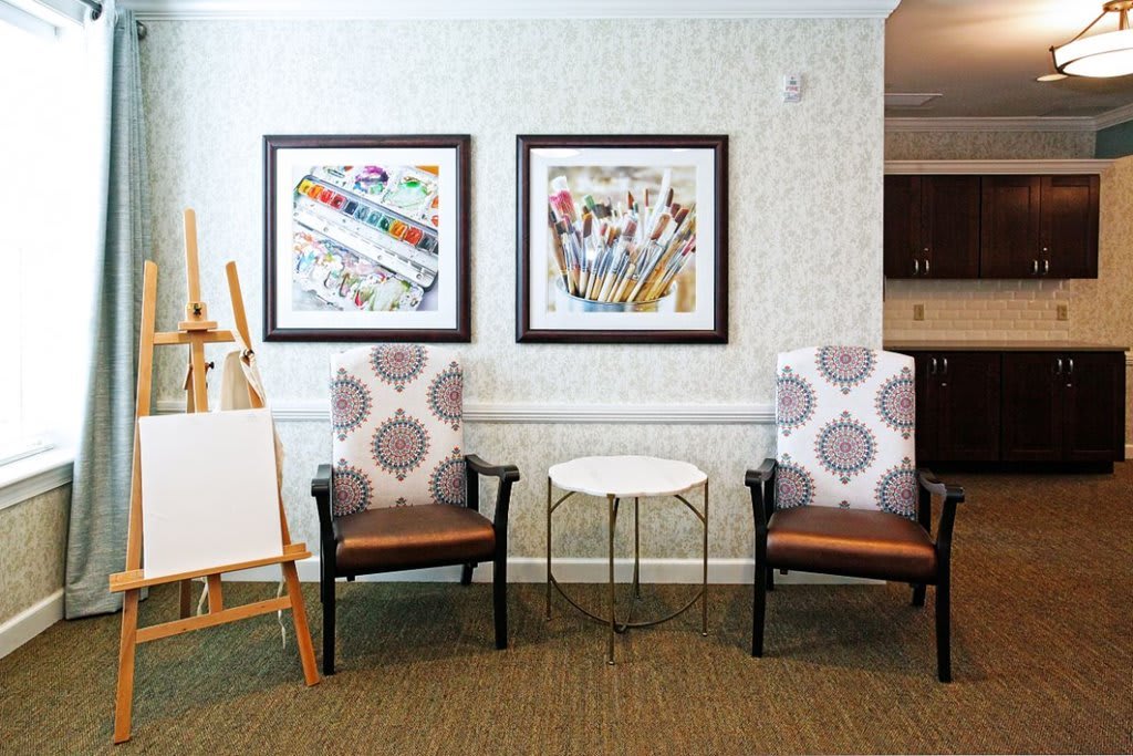 A cozy living room setup featuring two patterned chairs, artwork on the walls, and an easel for painting.