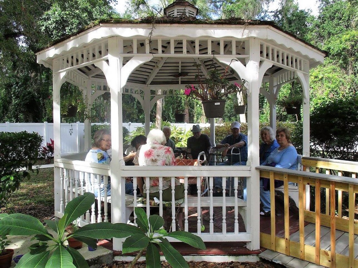 A group of people relaxing in a white gazebo surrounded by greenery.