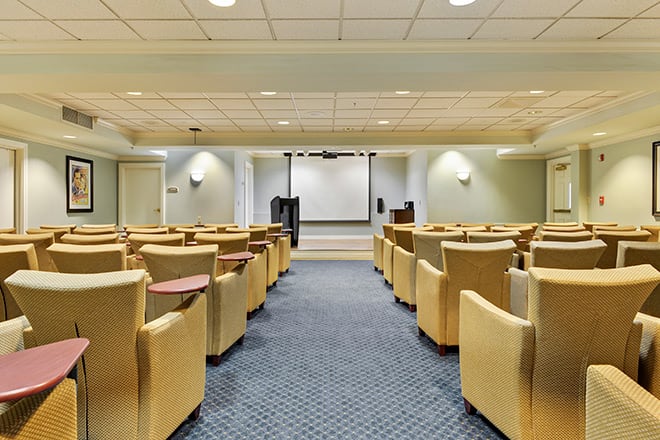 An empty auditorium with comfortable seating and a projector screen at the front.