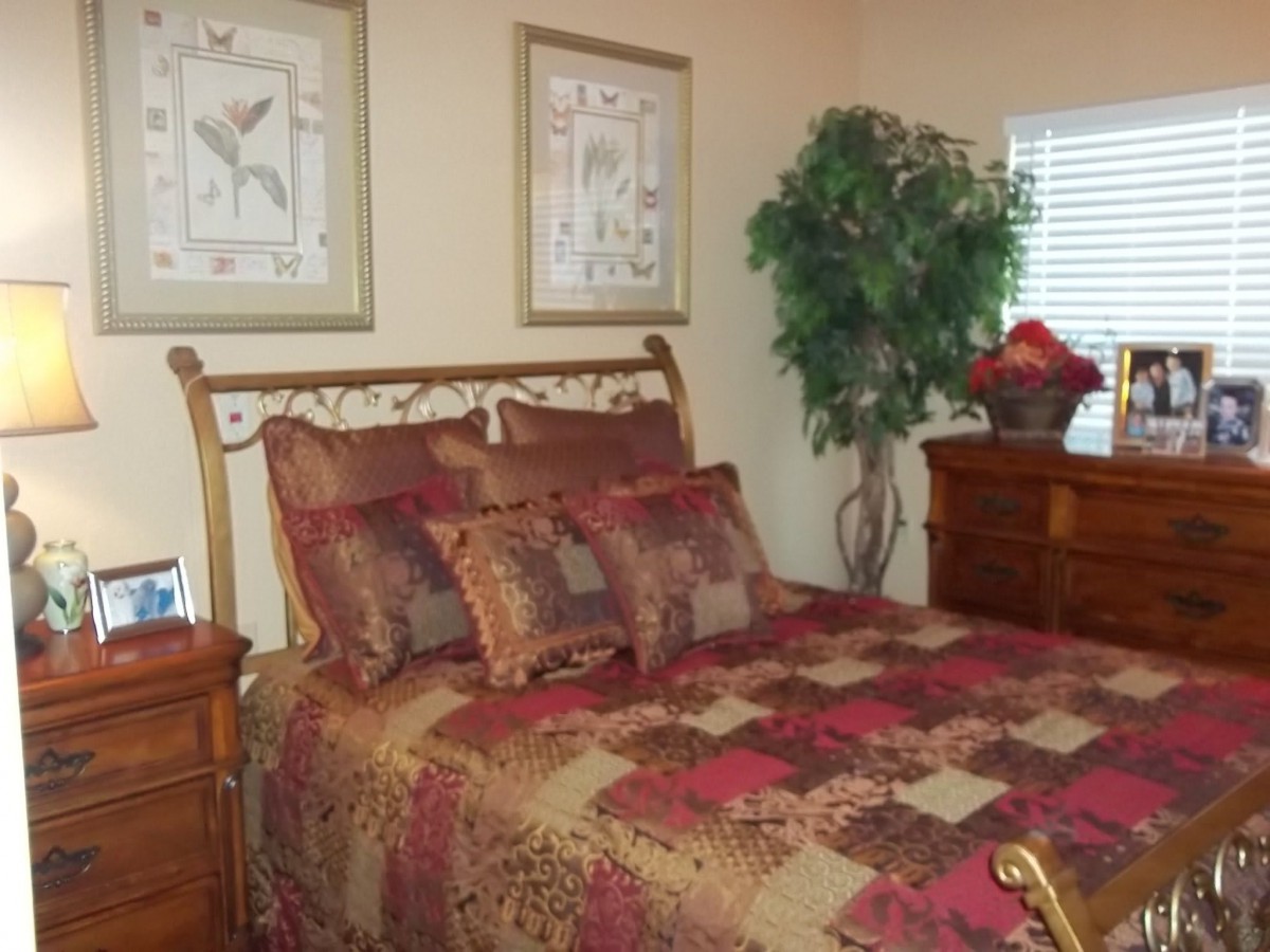 A cozy bedroom with a quilted bedspread and decorative pillows, featuring framed artwork and a potted plant.