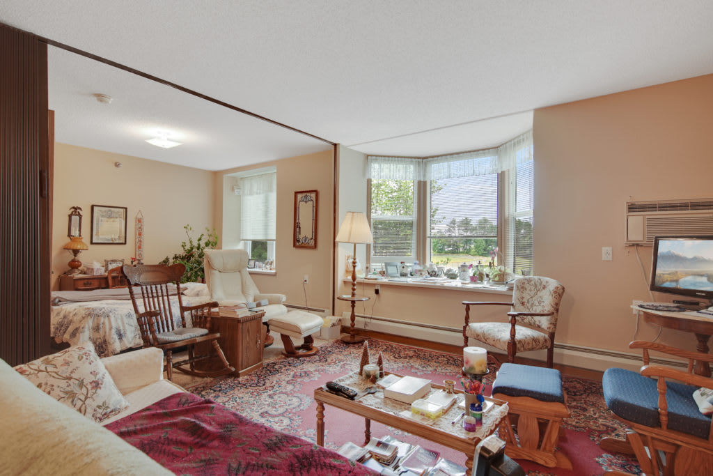A spacious living room with a large window, featuring comfortable seating and a cozy carpet.