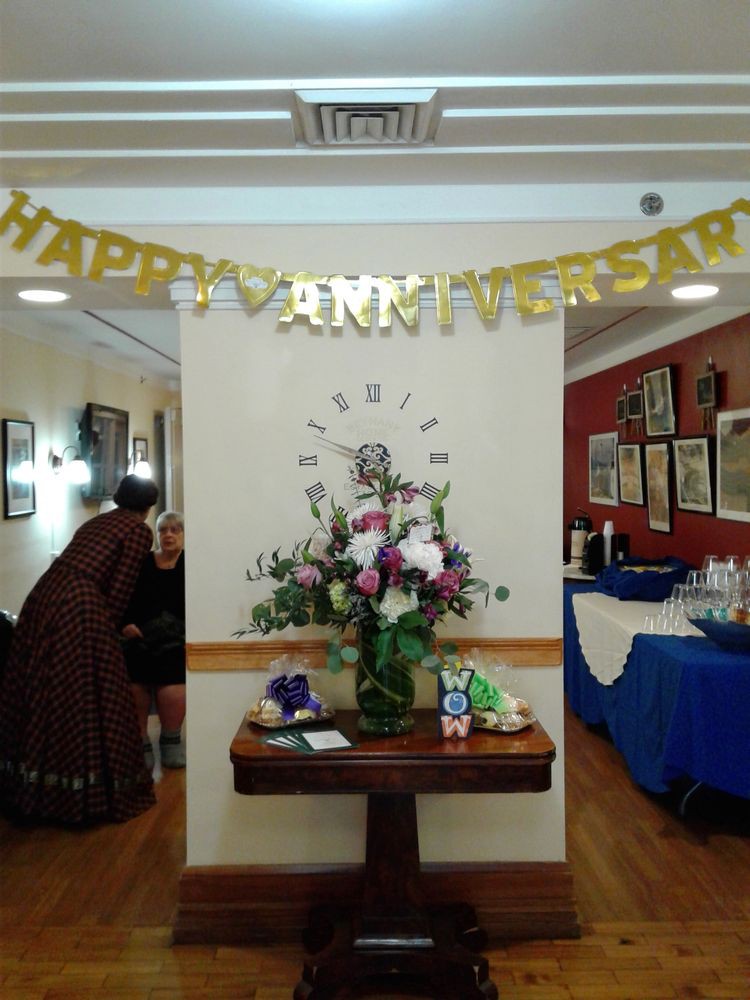 A festive setting for an anniversary party featuring a 'Happy Anniversary' banner and a floral arrangement on a table.