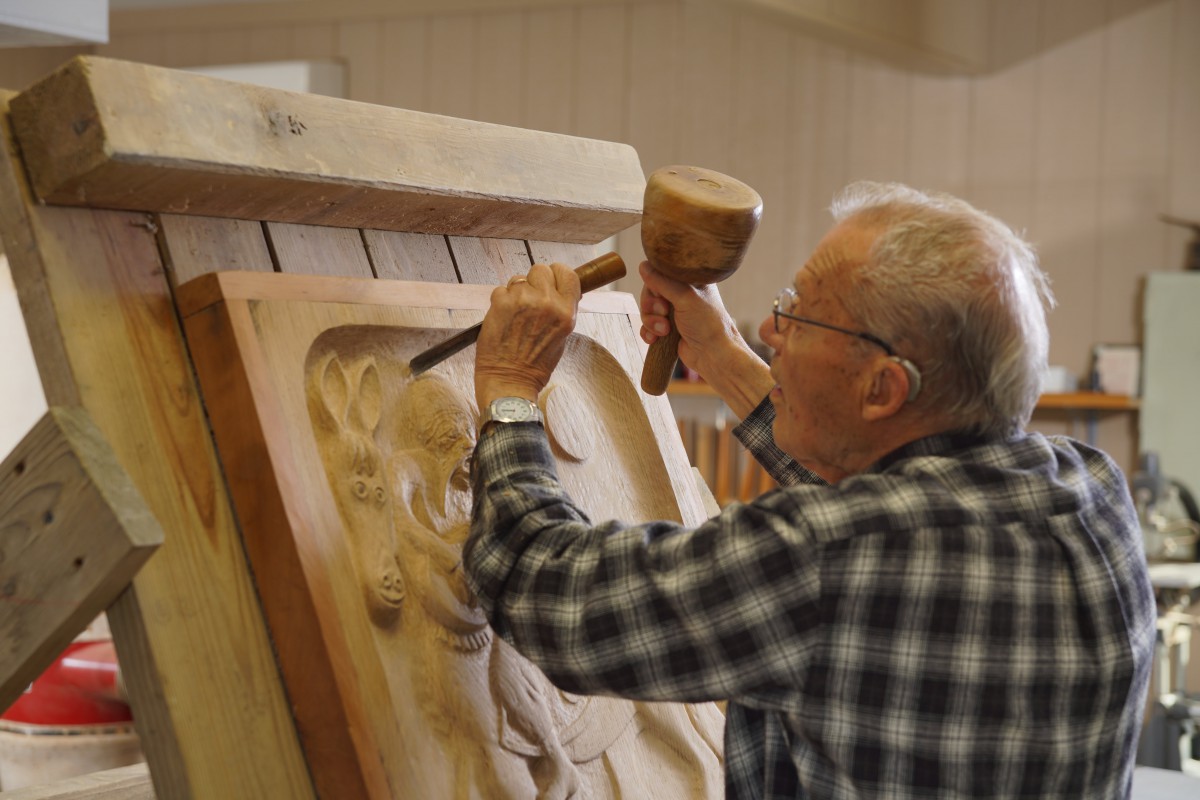 An artisan skillfully carves a detailed sculpture in wood using traditional tools.