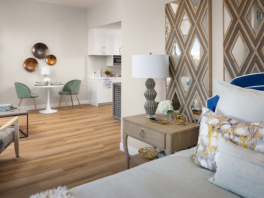 A modern interior featuring a cozy bedroom with stylish decor, a lamp on the nightstand, and a small dining area with contemporary chairs in front of a wooden floor.