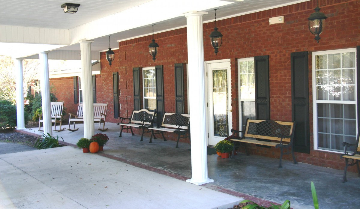 A cozy porch with chairs and autumn decorations, featuring columns and lantern-style lights.