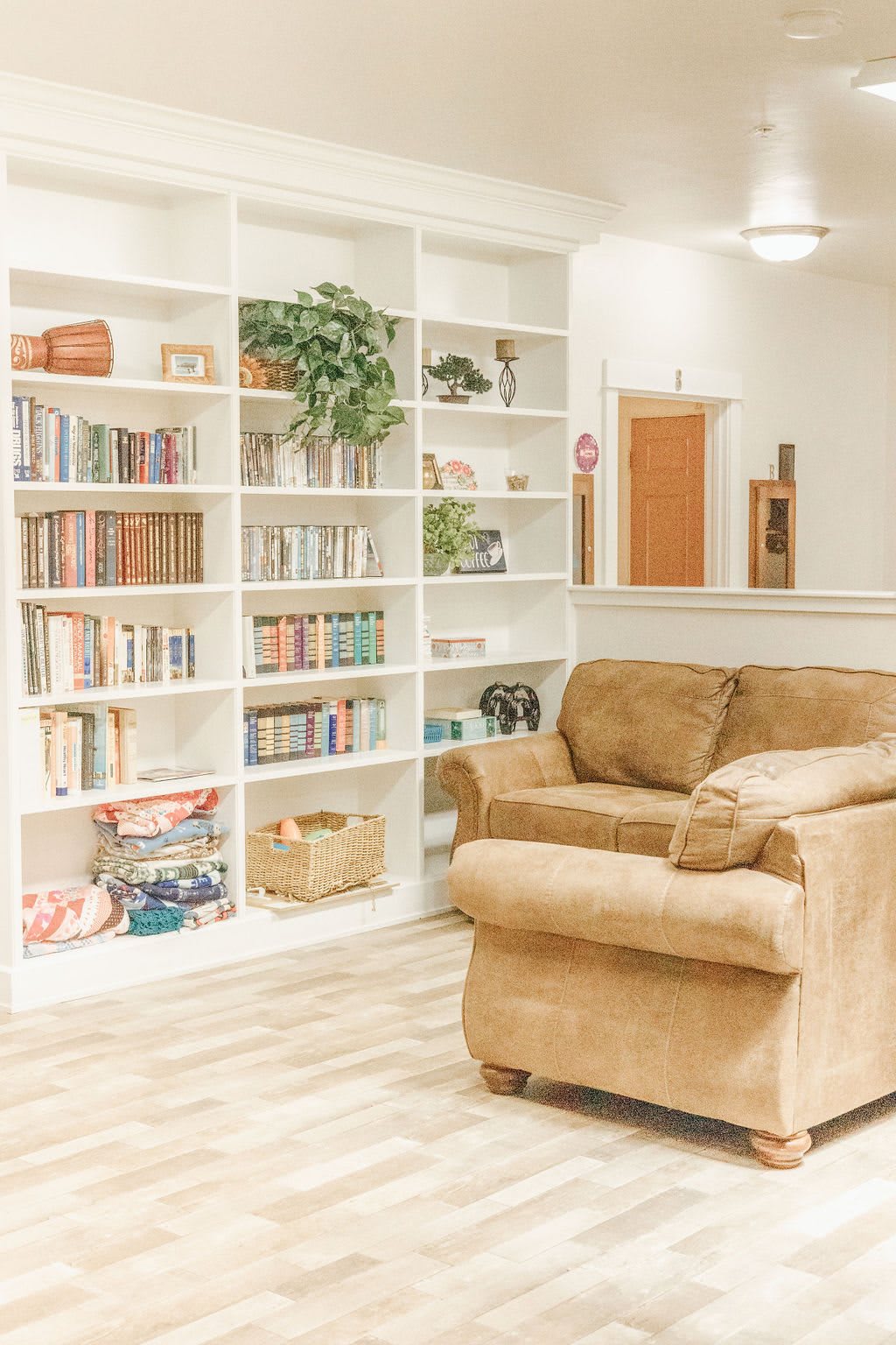 A cozy living room with a large bookshelf filled with books and decorations, next to a comfortable beige couch.