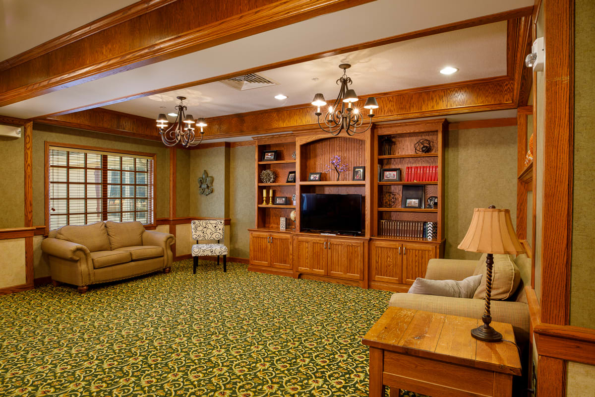 A cozy living room with wooden shelves and a television, featuring comfortable sofas and warm lighting.