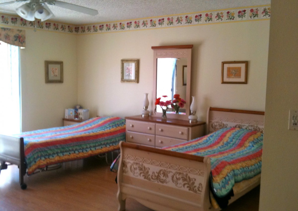 A cozy bedroom with twin beds adorned with colorful quilts, featuring a dresser with a mirror and floral decorations.