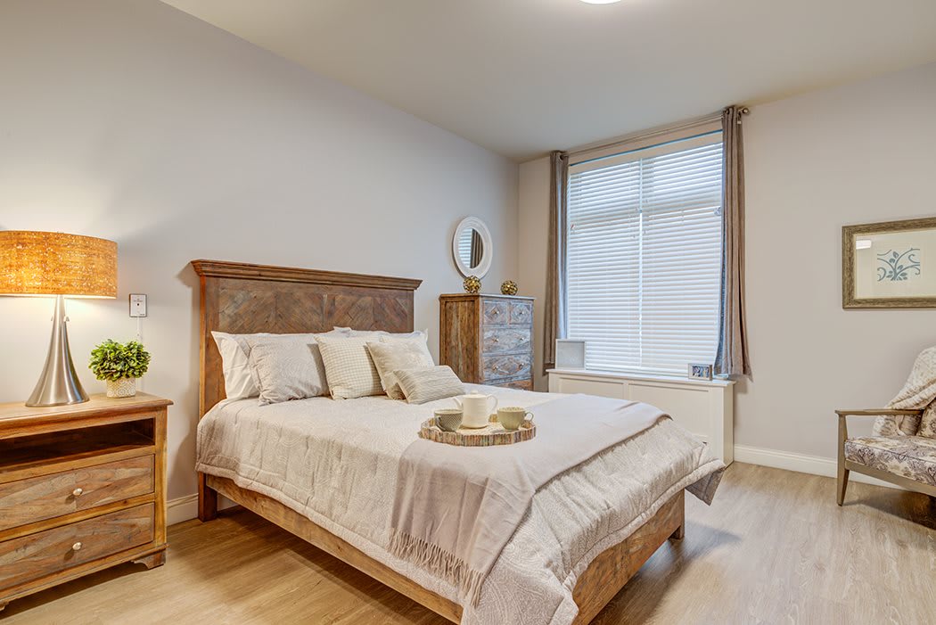 A cozy and modern bedroom featuring a neatly made bed with decorative pillows and a tray, surrounded by elegant furniture against a bright window.
