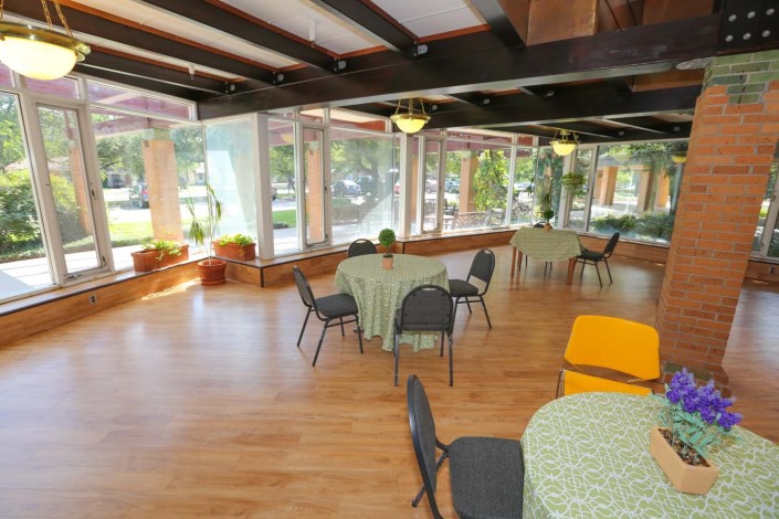 A spacious dining area with large windows, round tables, and wooden flooring.