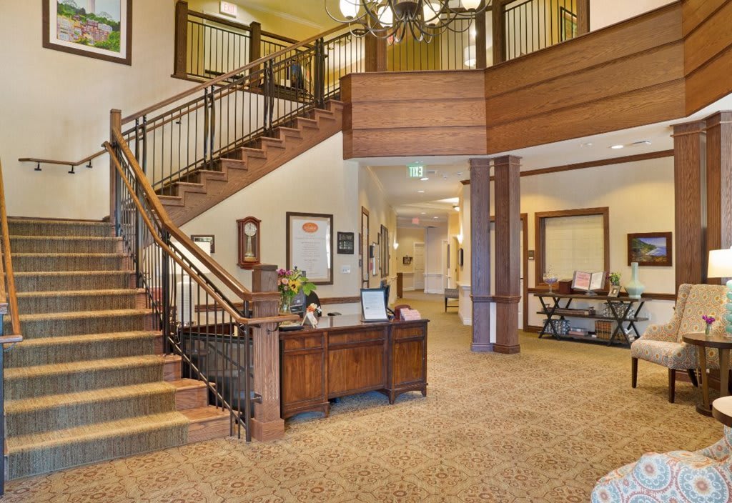 A spacious lobby area featuring a grand staircase with wooden railings, a reception desk, and elegant lighting.