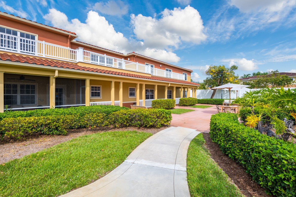 A residential building with a landscaped garden and pathway under a partly cloudy sky.