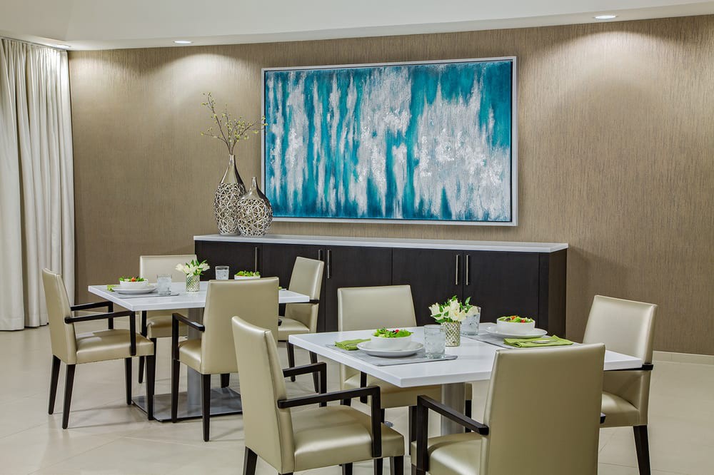 A modern dining room with elegant decor, featuring a large abstract painting and neatly arranged tables and chairs.
