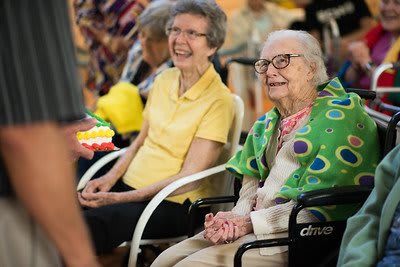 Two elderly women smiling and enjoying a community gathering indoors.