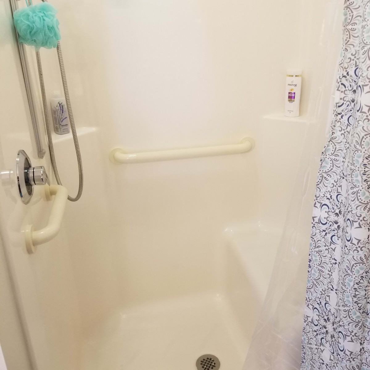 A clean bathroom shower with a handheld showerhead and grab bar.