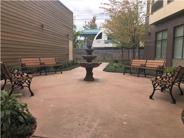 A peaceful courtyard with a central fountain, surrounded by benches and trees.