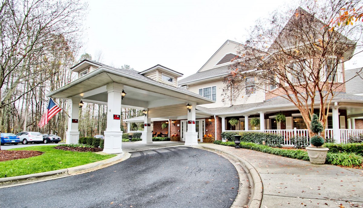 A welcoming entrance to a residential or hospitality building featuring a covered driveway and landscaped surroundings.
